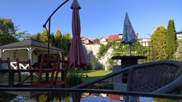 Vista clara de una piscina con el reflejo de un área de patio, que incluye una silla y una sombrilla.