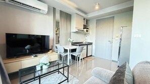 Una sala moderna con un televisor de pantalla plana, una mesa de centro de vidrio, un sofá y un comedor con una mesa y sillas blancas.
