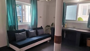 Ein Zimmer mit einer Couch, einem Fenster, einem Deckenventilator und einer Küchenzeile.