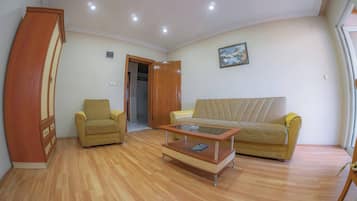 A living room with a sofa, armchair, and coffee table. There is a wooden wardrobe and a door leading to another room.