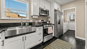Una cocina moderna con armarios blancos, electrodomésticos de acero inoxidable y piso de baldosas negras.