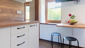 A kitchen with white cabinets, a wooden countertop, a window with a view of greenery, and a small table with stools. - Apartment Arnika by Interhome (Janov nad Nisou)
