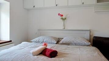A neatly made bed with striped bedding, a vase with flowers, and a red towel on the bed.