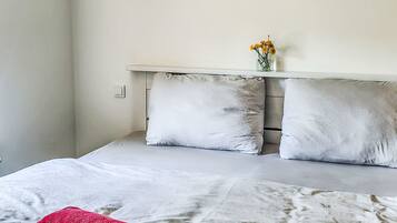 A bedroom with a bed, pillows, a bedside table with a vase of flowers, and a red towel.