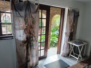 A room with a view of a garden through a doorway, a small table with plates, and a doormat. - Character Cottage with Balcony in Peaceful Garden (Johannesburg)