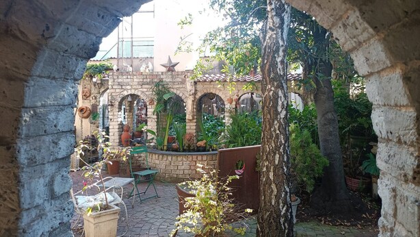 Une cour extérieure agrémentée d’une arche en pierre, de plantes en pot et d’un mur en briques.