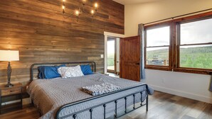 Quarto com parede de madeira, cama com estrutura metálica, mesa de cabeceira, luminária e janela com vista.