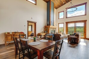 A spacious dining area with a wooden table and chairs, a fireplace, and large windows offering a view of the outdoors. - On 7 Acres! Scenic Home w/ Game Room in Fairplay (Fairplay)