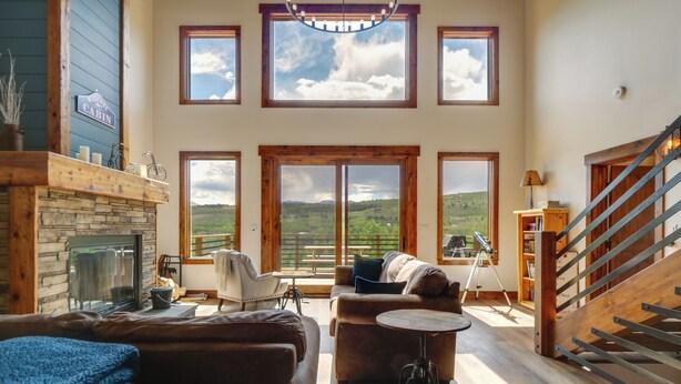 Uma sala de estar ampla com lareira, janelas grandes, escada e vista para o exterior.