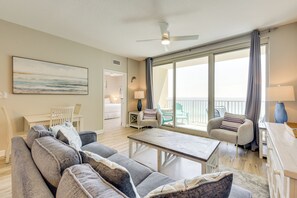 Un salon spacieux avec un grand canapé, une table basse et une vue sur l’océan grâce à de grandes fenêtres.