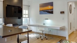 Una cocina moderna con un televisor de pantalla plana grande, una mesa de comedor con sillas, una encimera blanca y un escritorio de cristal con una silla.