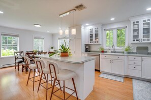 A modern kitchen with white cabinetry, a central island with bar stools, and pendant lighting. - Serene & Sleek Family Retreat w/ Office in Shirley (Shirley)