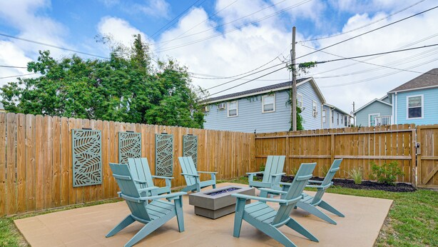 A backyard with a wooden fence, a fire pit, and four Adirondack chairs. - 1 Block to Beach: Fire Pit, Outdoor Kitchen, Bikes (Galveston)