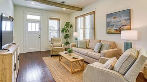 A living room with a sofa, armchairs, a coffee table, a TV, and a painting on the wall. - 1 Block to Beach: Fire Pit, Outdoor Kitchen, Bikes (Galveston)