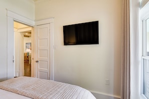 Ein Schlafzimmer mit einem Bett, einem Fernseher an der Wand und einer Tür zu einem anderen Raum.