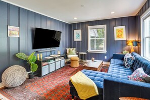 A living room with a flat-screen TV, a blue sofa, a patterned rug, and a window with a view. - 2 Mi to UNC Campus! Quiet Escape w/ Deck & Grill (Carrboro)