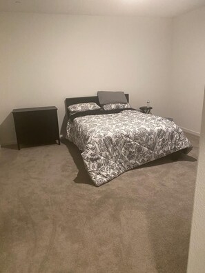 A bedroom with a bed, two nightstands, a small table, and a carpeted floor. - Serene 4-bedroom building with AC in charming Patterson (Patterson)