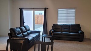 Un salon avec deux canapés en cuir noir, une table à manger en bois avec des chaises, un ordinateur portable et une souris sur un tapis de souris.
