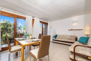 A dining area with a wooden table and chairs, a sofa, and a view of greenery outside. - Da Marta 10 Passi Dal Mare (Arzachena)