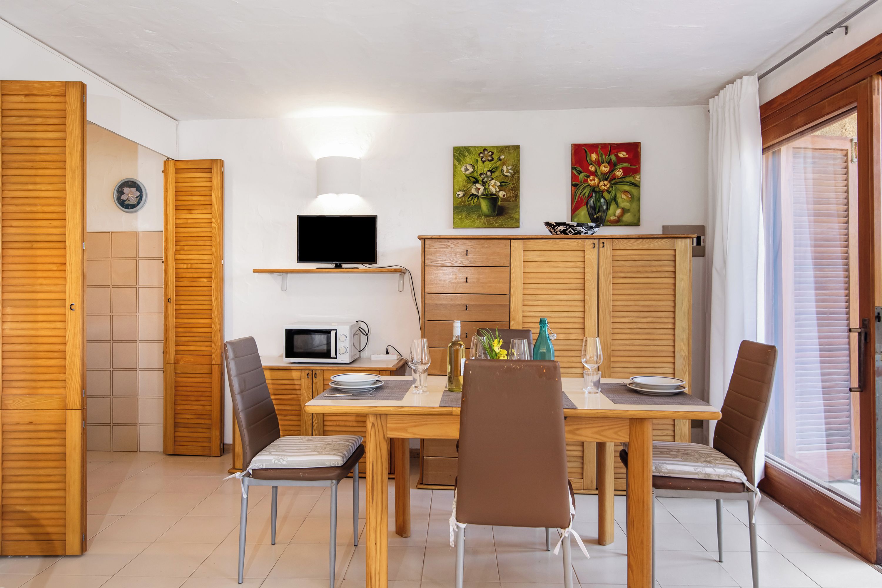 A dining area with a wooden table, chairs, a TV, and artwork on the wall.