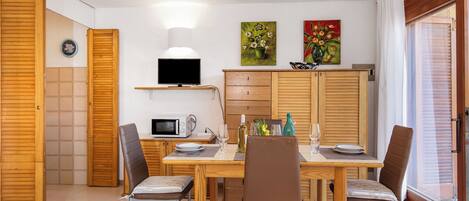 A dining area with a wooden table, chairs, a TV, and artwork on the wall.