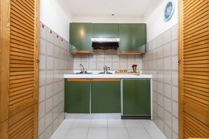 A compact kitchen with green cabinets, a white countertop, a stainless steel range hood, and a clock on the wall. - Da Marta 10 Passi Dal Mare (Arzachena)