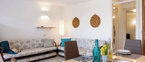A dining area with a table set for four, a sofa, and a wall-mounted shelf.