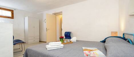 Une chambre à coucher comprenant un lit, une chaise, une armoire et une porte donnant sur une autre pièce.