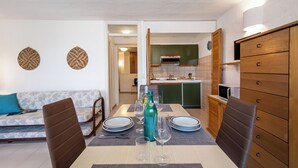 Un coin repas avec une table dressée pour quatre personnes, un canapé et une cuisine en arrière-plan.