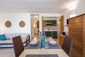 Un comedor con una mesa lista para cuatro personas, un sofá y una cocina al fondo.