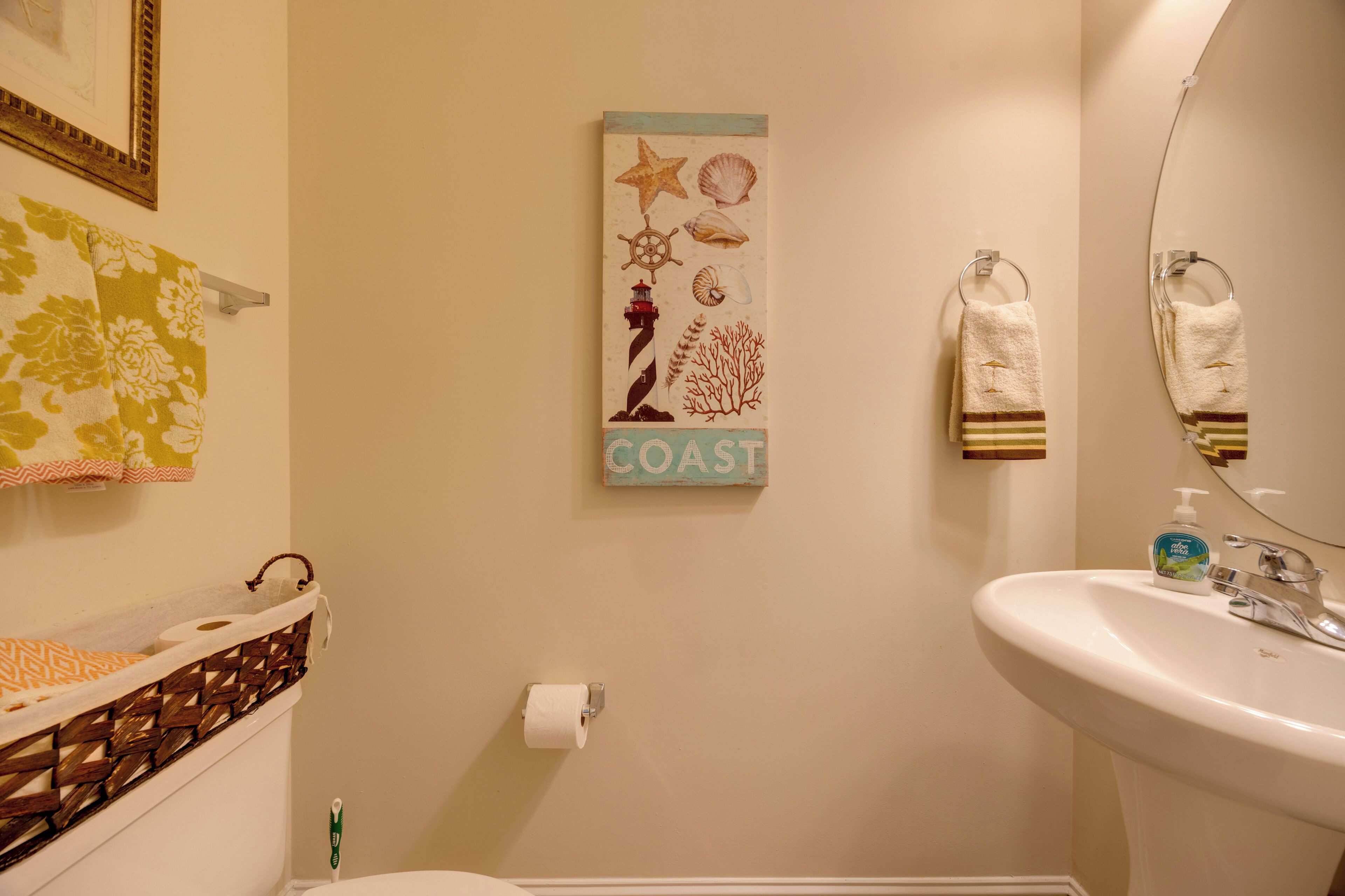 A bathroom with a toilet, a sink, a towel rack, and a wall decoration with maritime elements.