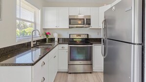 Una cocina moderna con armarios blancos, electrodomésticos de acero inoxidable, encimera de granito y una ventana con persianas.