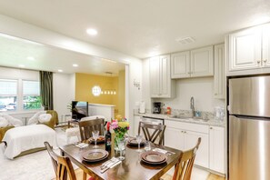 A modern kitchen with white cabinets, a stainless steel refrigerator, and a dining area with a wooden table set for four. - Explore Oberlin! Home 1 Mi to Main Street & Campus (Oberlin)