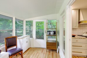 A kitchen with white cabinets, a wooden chair, a microwave, and a view of greenery outside. - Explore Oberlin! Home 1 Mi to Main Street & Campus (Oberlin)