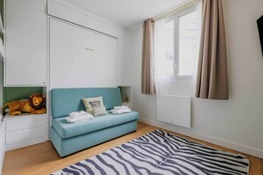 Een kamer met een smaragdgroene bank, een vloerkleed met zebraprint, een leeuw decoratie, een raam met gordijnen en een radiator.