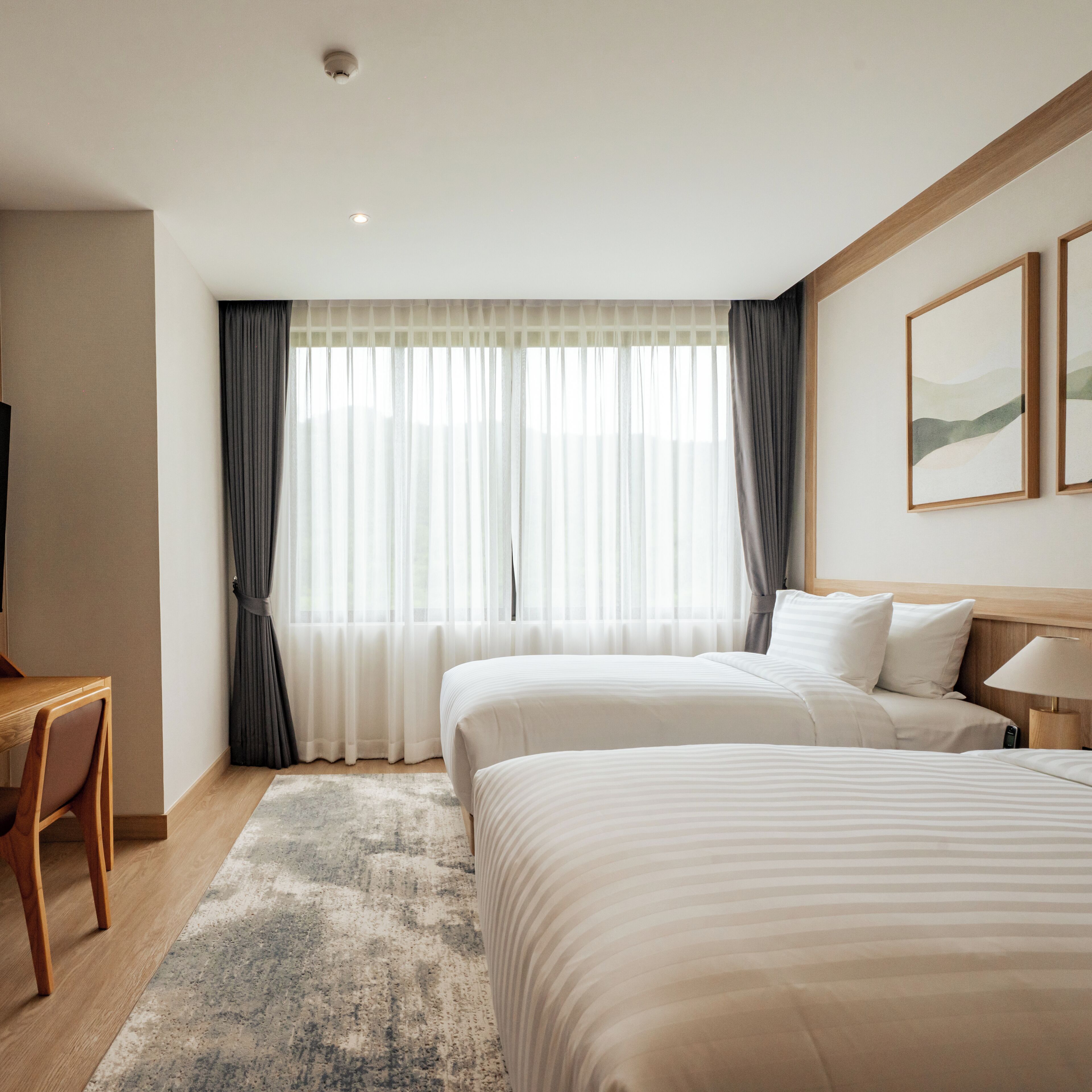 Habitación de hotel con dos camas, un escritorio y un ventanal grande con cortinas.