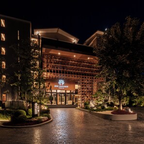 Entrada de hotel con diseño moderno, un cartel y un camino bien iluminado hacia la entrada.
