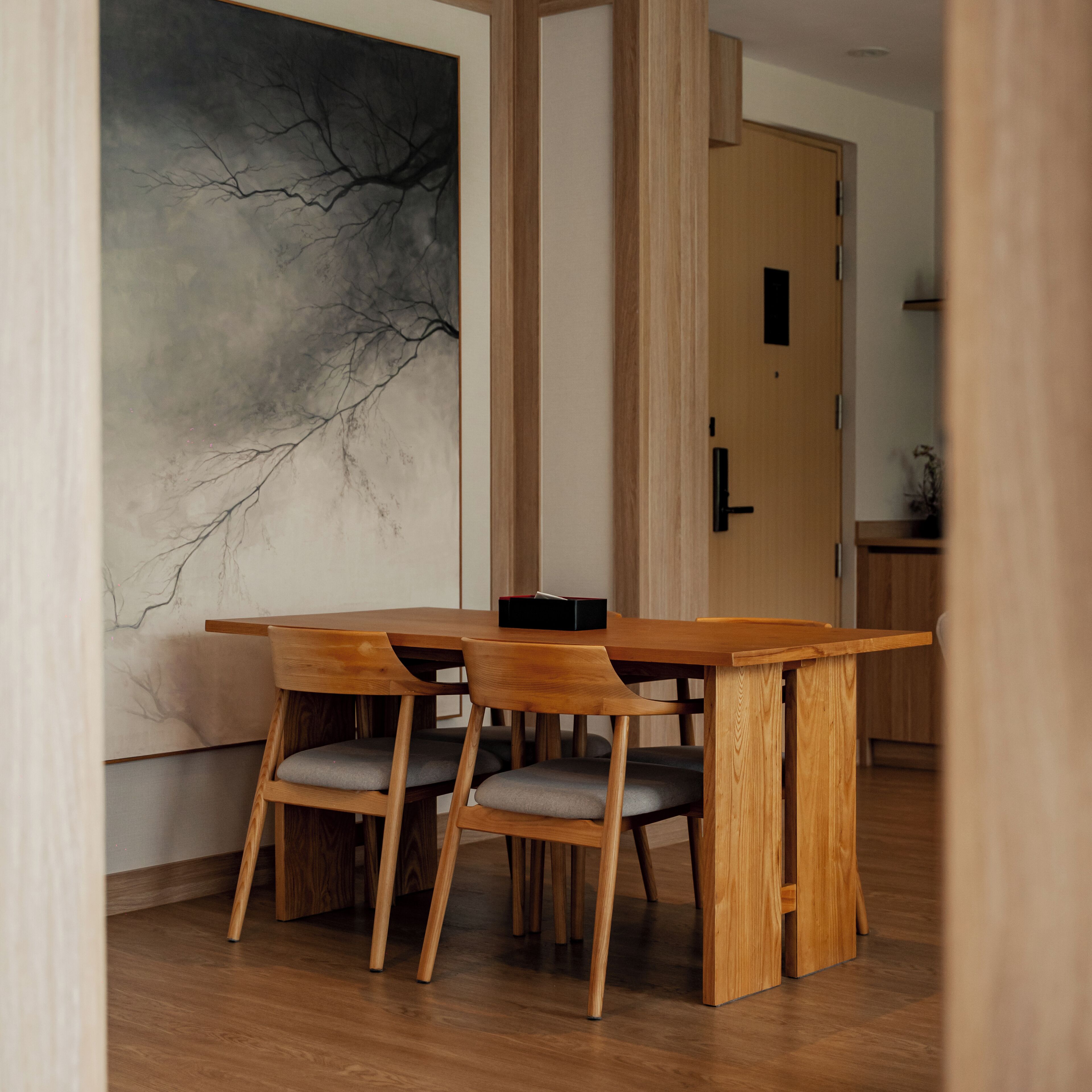 A dining area with a wooden table and chairs, a large abstract painting on the wall, and a wooden door in the background.