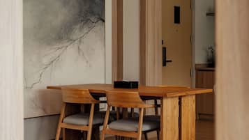 A dining area with a wooden table and chairs, a large abstract painting on the wall, and a wooden door in the background.