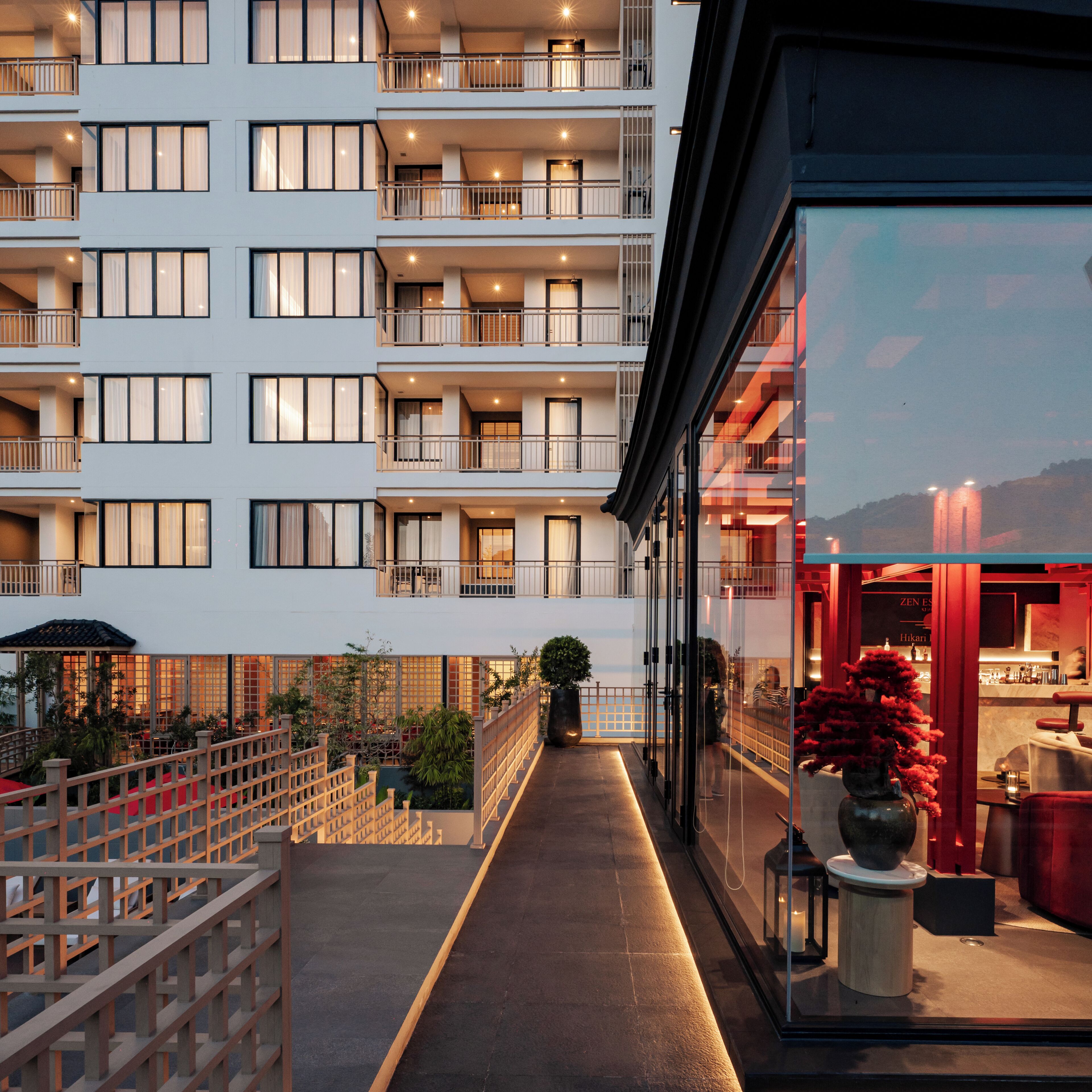 A multi-story hotel with balconies, a covered outdoor area with plants, and a restaurant visible through the glass facade.