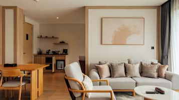 A modern living room with a sofa, armchairs, a coffee table, and a dining area with a wooden table and chairs.