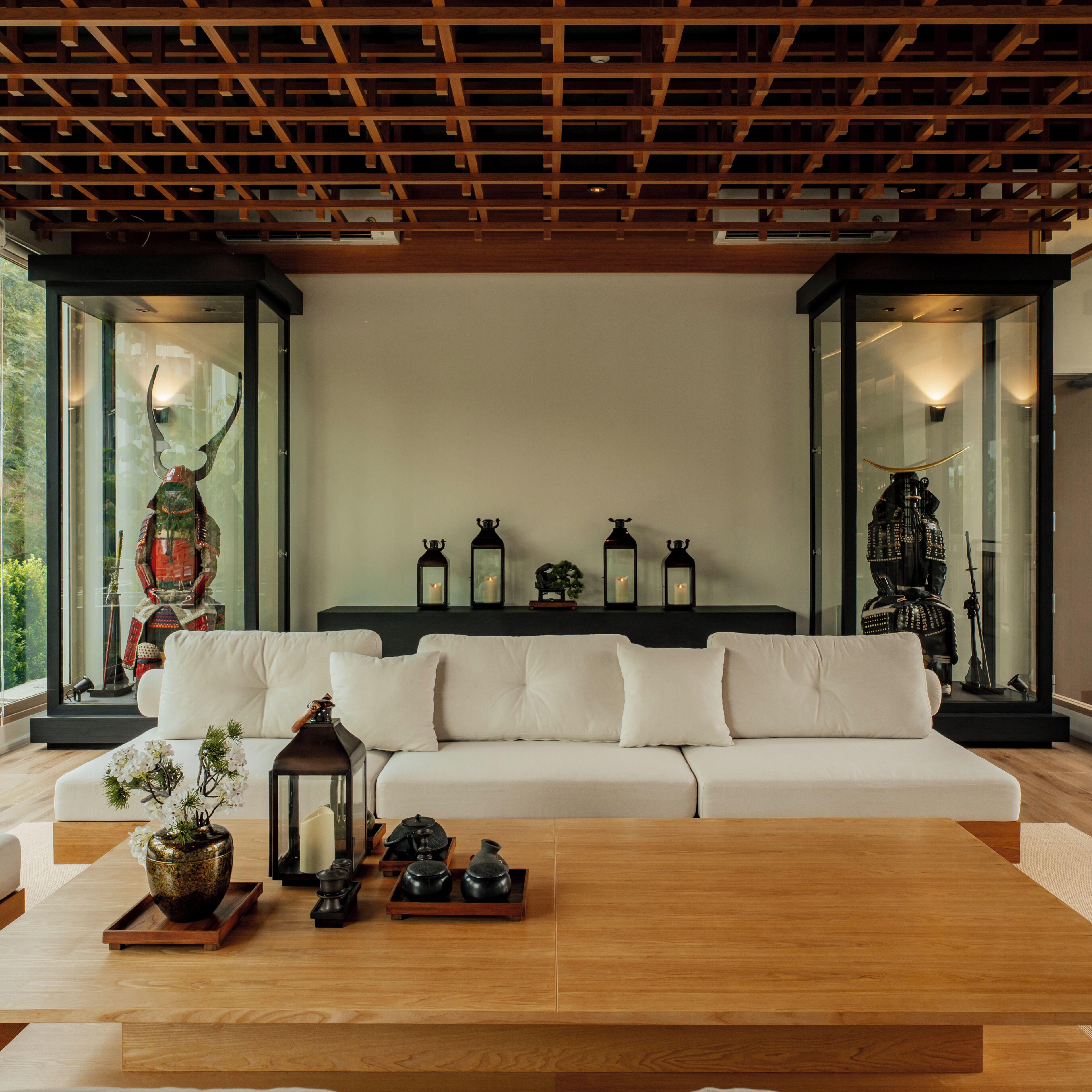 Uma sala de estar moderna com teto de madeira, um sofá branco e objetos decorativos, incluindo uma estátua, lanternas e um vaso.
