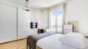 Hotellihuone, jossa on sänky, televisio, työpöytä, vaatekaappi ja ikkuna, josta on näkymä.