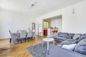 Ein modernes Wohnzimmer mit grauem Sofa, einem Esstisch mit Stühlen und einem durch einen offenen Durchgang einsehbarer Küchenbereich.