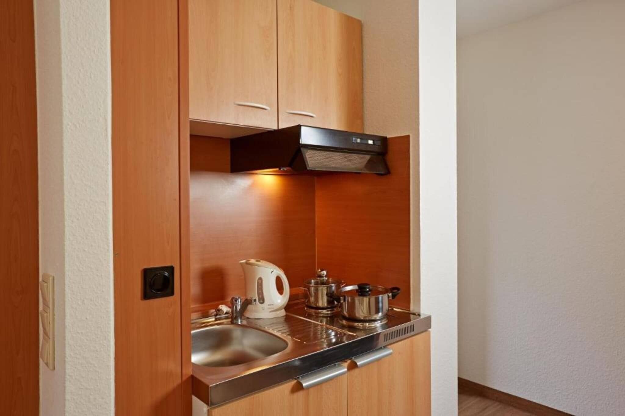 Een kleine keuken met houten kastjes, een roestvrijstalen spoelbak en een waterkoker.