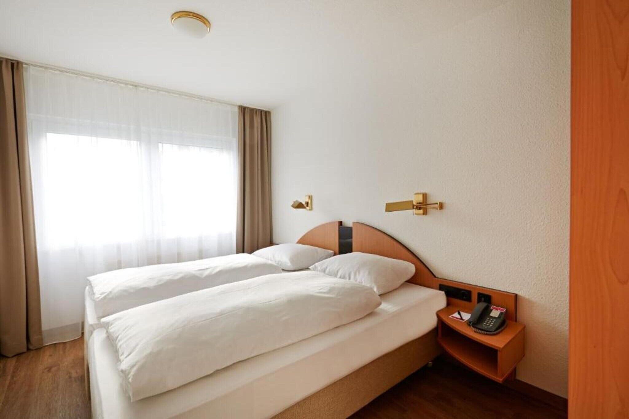 A hotel room with two beds, a bedside table with a phone, and a window with curtains.