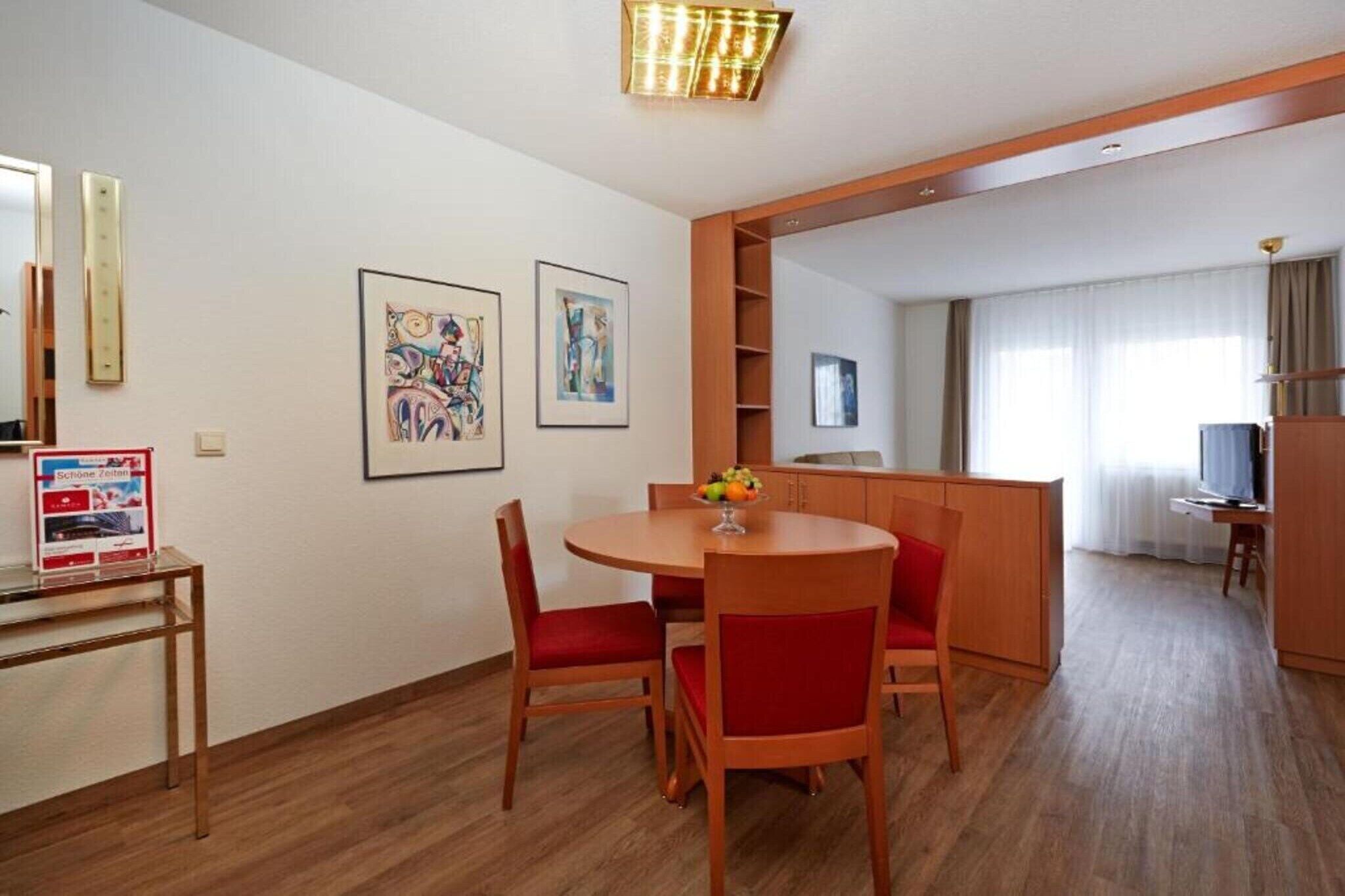 Habitación de hotel con comedor, televisor y obras de arte en las paredes.