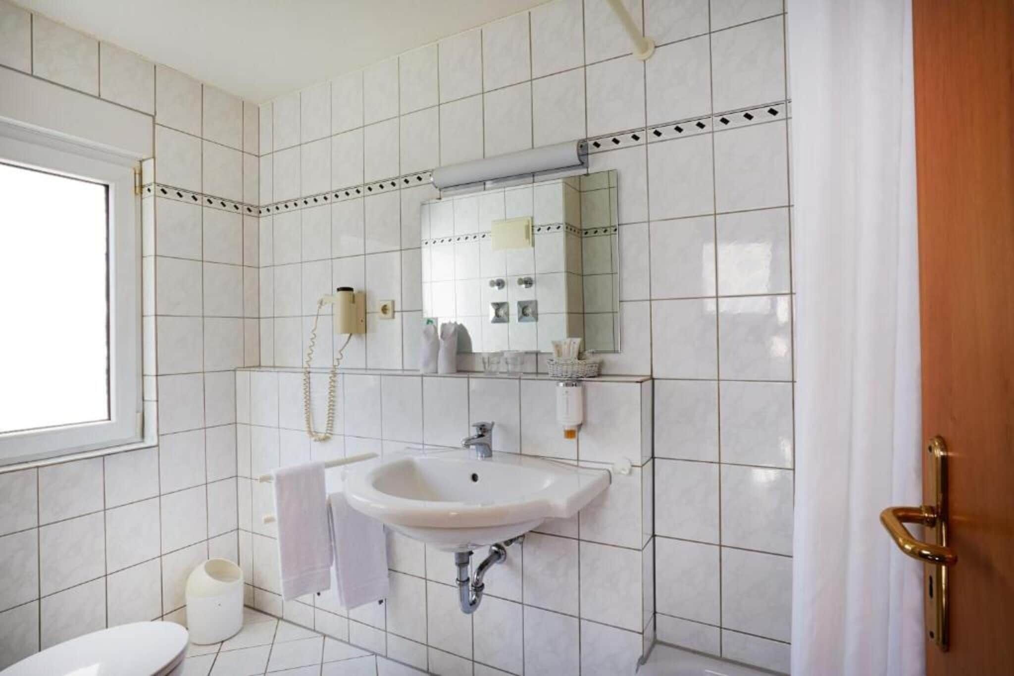 Un baño con azulejos blancos, un lavabo, un espejo y un inodoro.