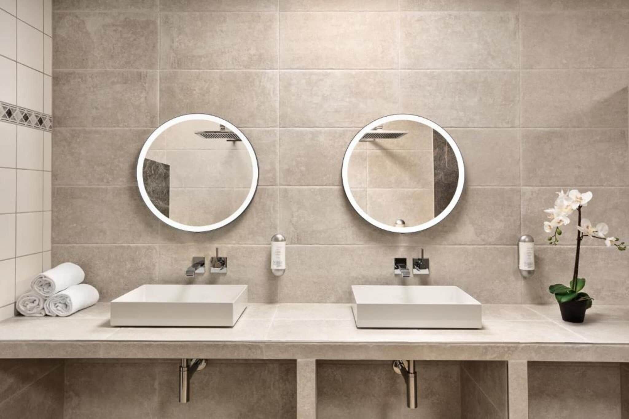 Ein Badezimmer mit zwei Waschbecken, jeweils mit einem Spiegel darüber. Auf der Ablage liegen Handtücher und ein Blumentopf.