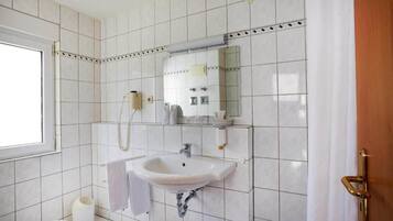 Un baño con azulejos blancos, un lavabo, un espejo y un inodoro.